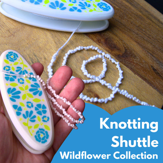 Knotting shuttle with floral design held by a hand, on a wooden surface with text 'Knotting Shuttle Wildflower Collection'.