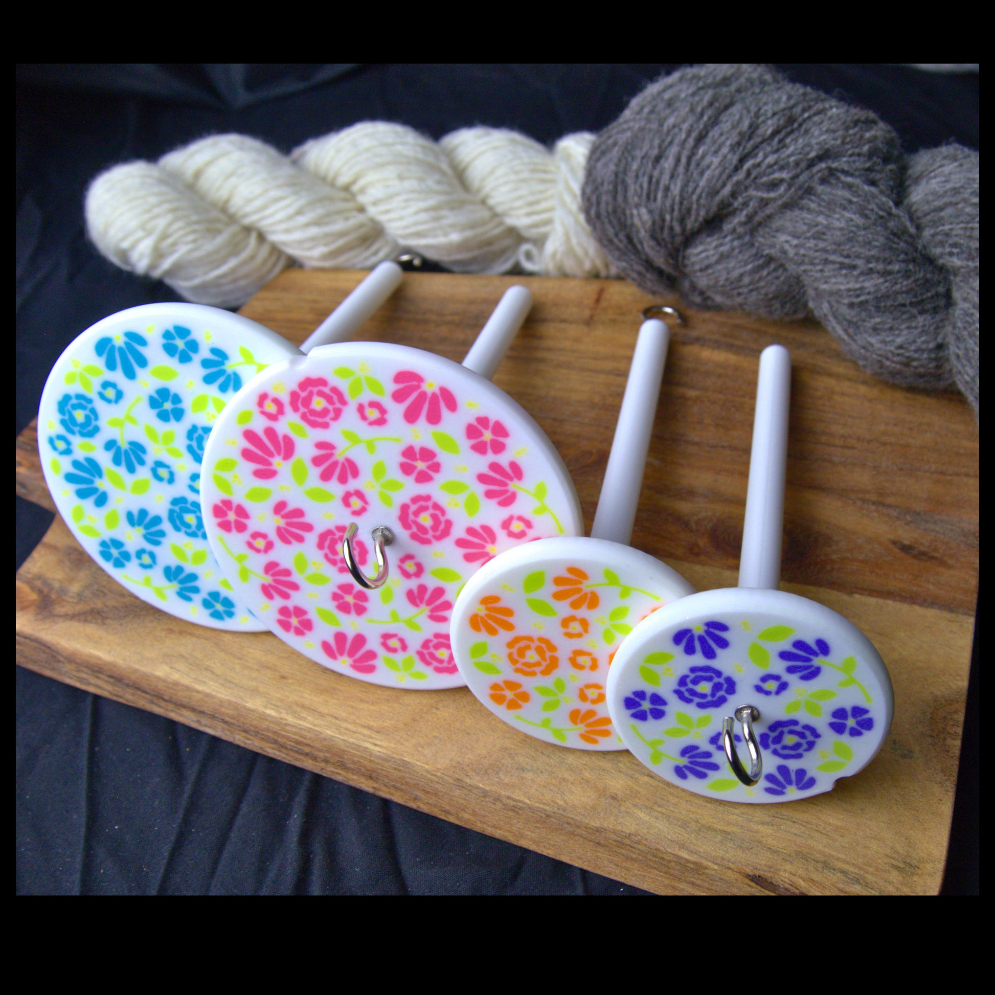four drop spindles in differeny sizes and weight setups alongside some cream and grey handspun yarn skeins