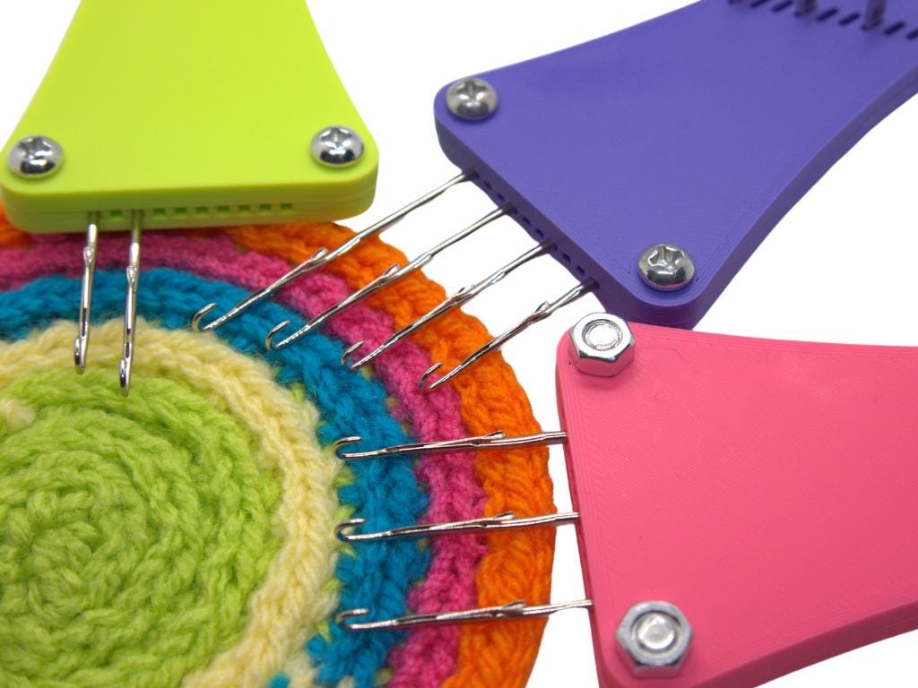 Colorful adjust-a-cord cord making tools in lime, purple and pink on a placemat they knitted themselves